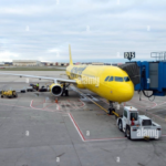 img_9482-1 - NubianBiz | African Business Directory, Jobs, Marketplace & Entrepreneur Insights Yellow passenger jet at gate d15 connected to jet bridge on tarmac, ground crew vehicles nearby.