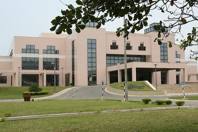 img_9505 - NubianBiz | African Business Directory, Jobs, Marketplace & Entrepreneur Insights Exterior view of a large beige modern building with tall glass windows and a curved driveway, surrounded by green lawn.